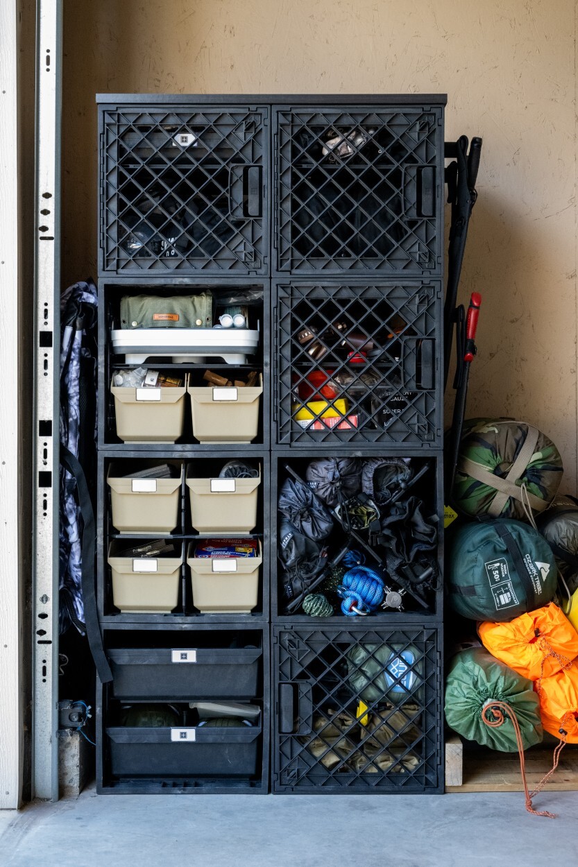UbeCube crate tower near a garage door organizing camping gear with bins, shelves, trays, soft outdoor bags, and visible crate compartments.