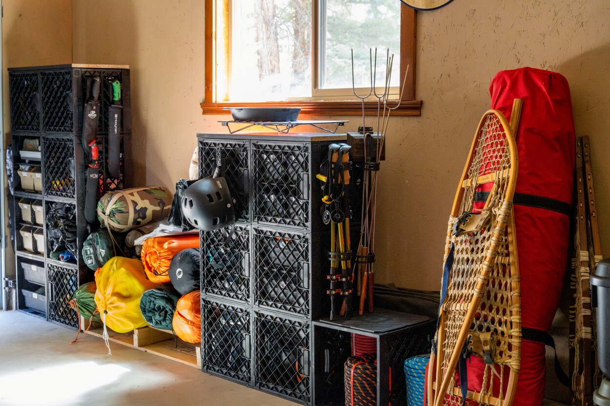 Garage camping gear organization system with stacked UbeCube crates, sleeping bags, trekking poles, snowshoes, helmets, and outdoor supplies.