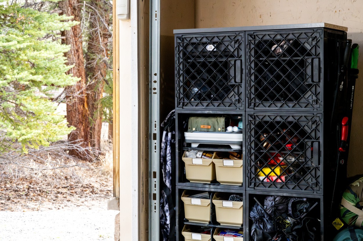 Tall UbeCube crate storage tower organizing camping gear, Grab Bins, trays, ropes, sleeping bags, and outdoor supplies near a garage entrance.