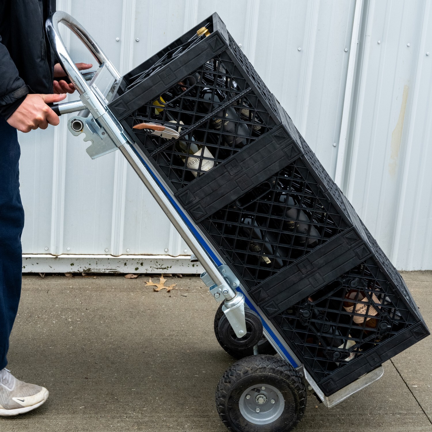 Man pushing dolly with three UbeCube Crates stacked and ouftitted with CrateWine Dividers, organizing 12 wine bottles each. On the side of the stack are Magnet Clip attachments attached via the diamond lattice on the side of the crate, holding wine openers.