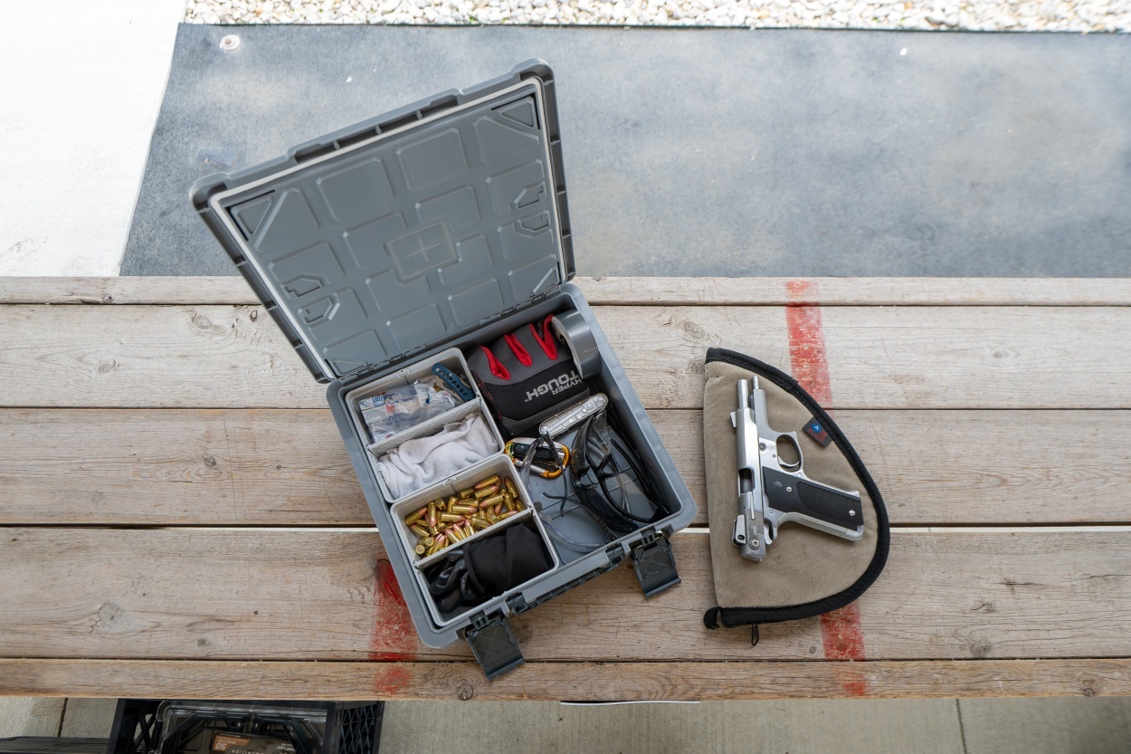 CrateShot storage box with organized ammo and gear next to a handgun at an outdoor shooting range setup