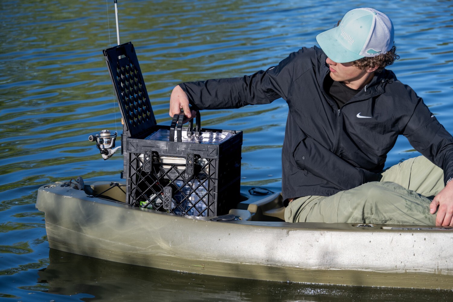 Kayak angler lifting a BaseBox tackle organizer from an open black PaddleOn crate while seated on the water.