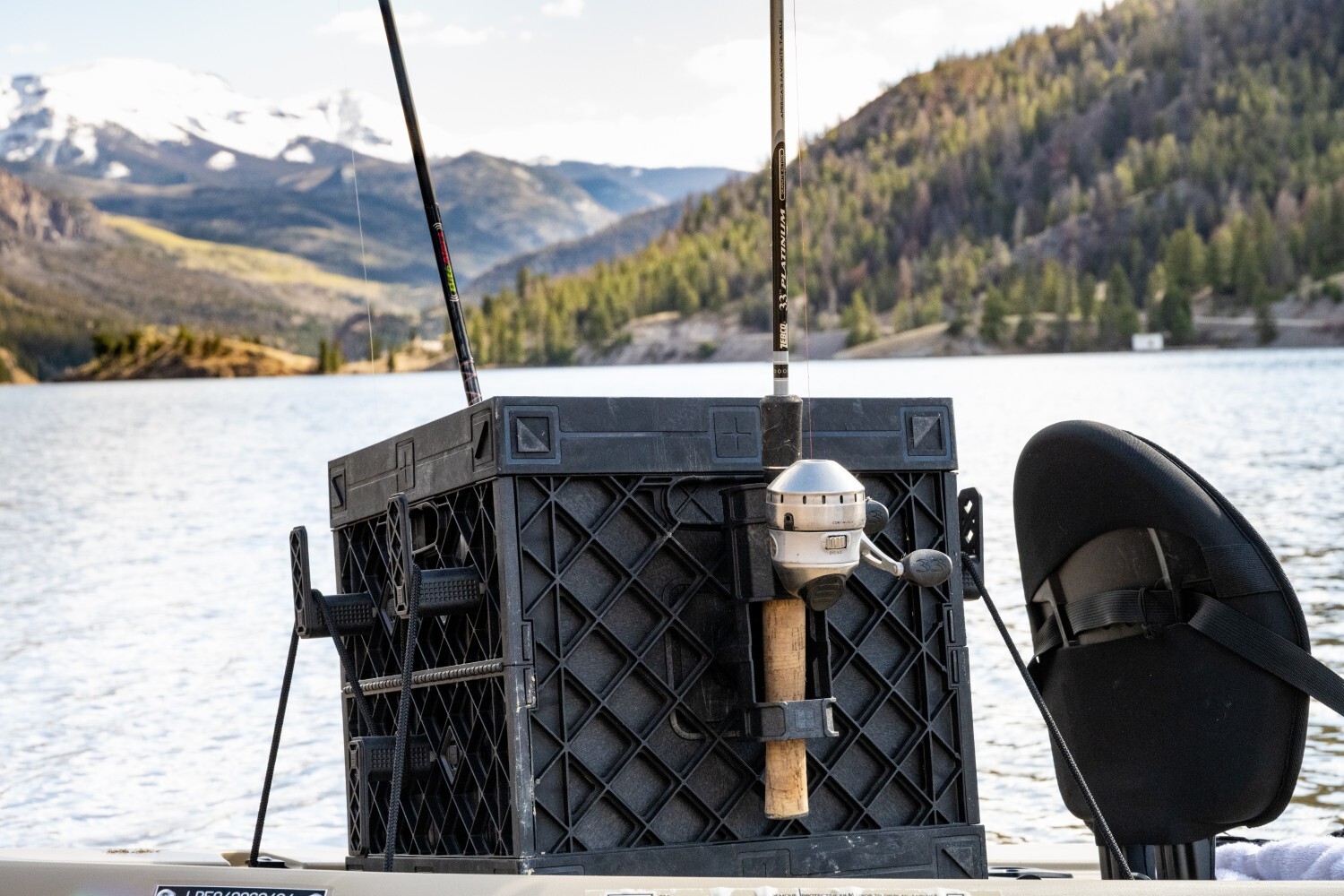 Rear view of a PaddleOn crate holding two fishing rods on a kayak overlooking a mountain lake.