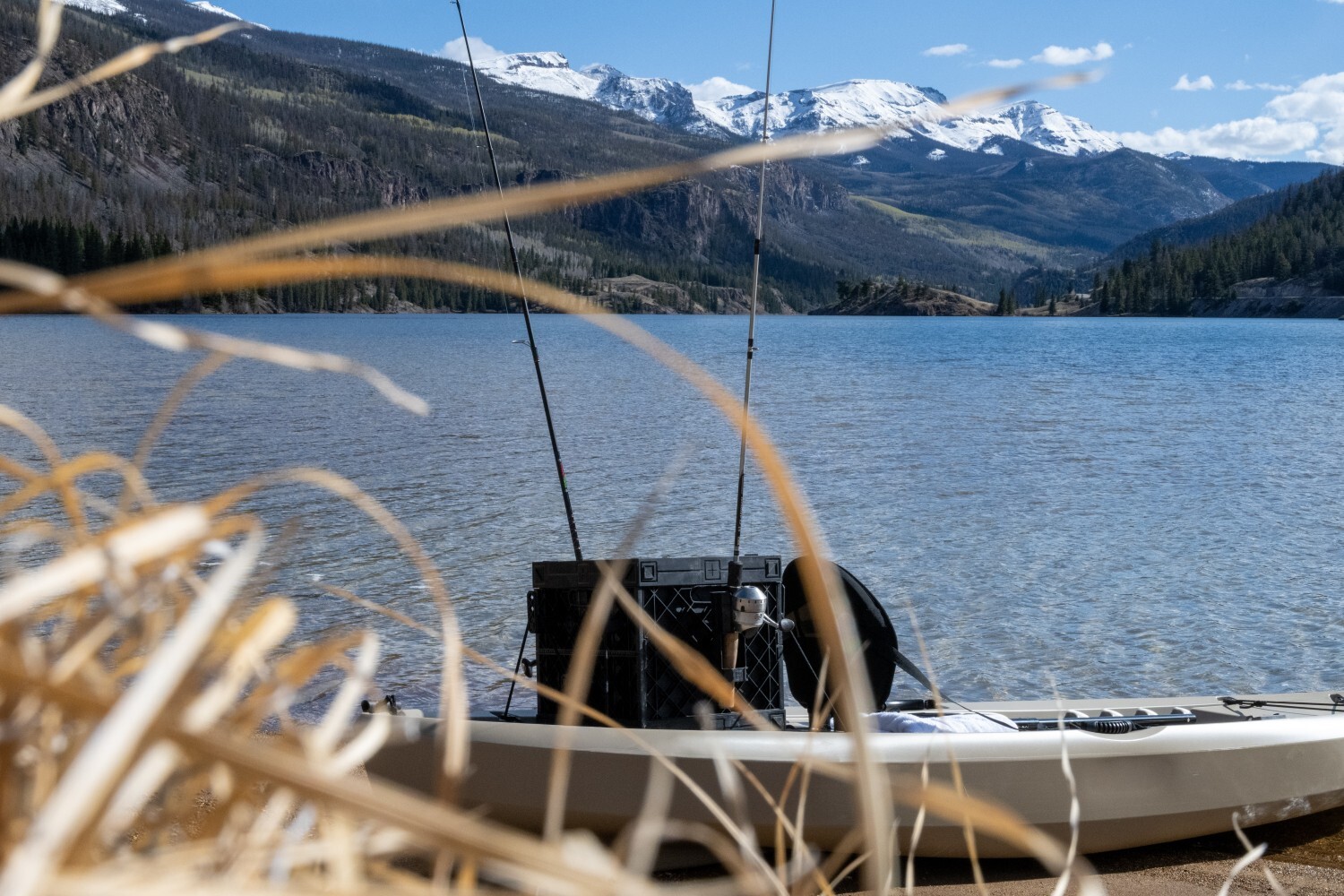 Fishing kayak with a PaddleOn crate and upright fishing rods resting beside a mountain lake.