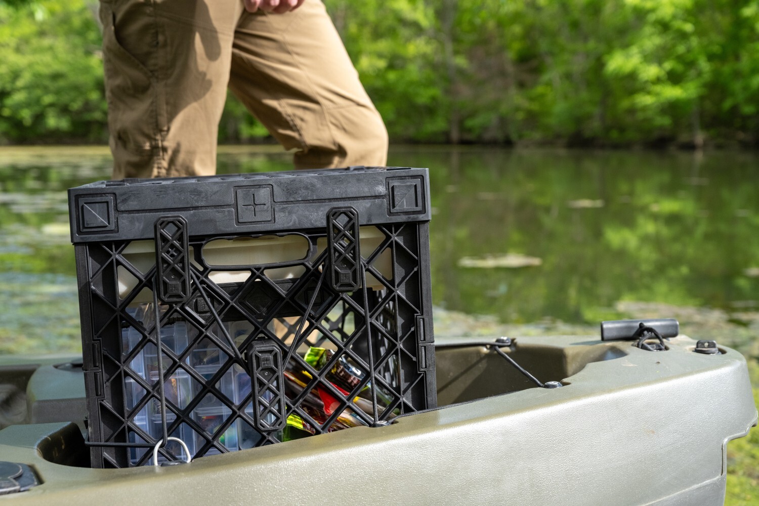 Black PaddleOn fishing crate secured in the rear tank well of a green kayak beside the water.